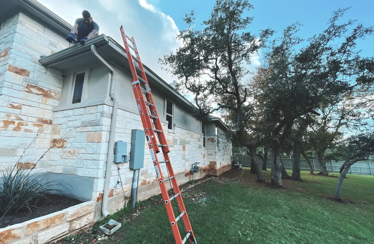 Urtiz crew member on roof during inspection at Texas stone home with ladder