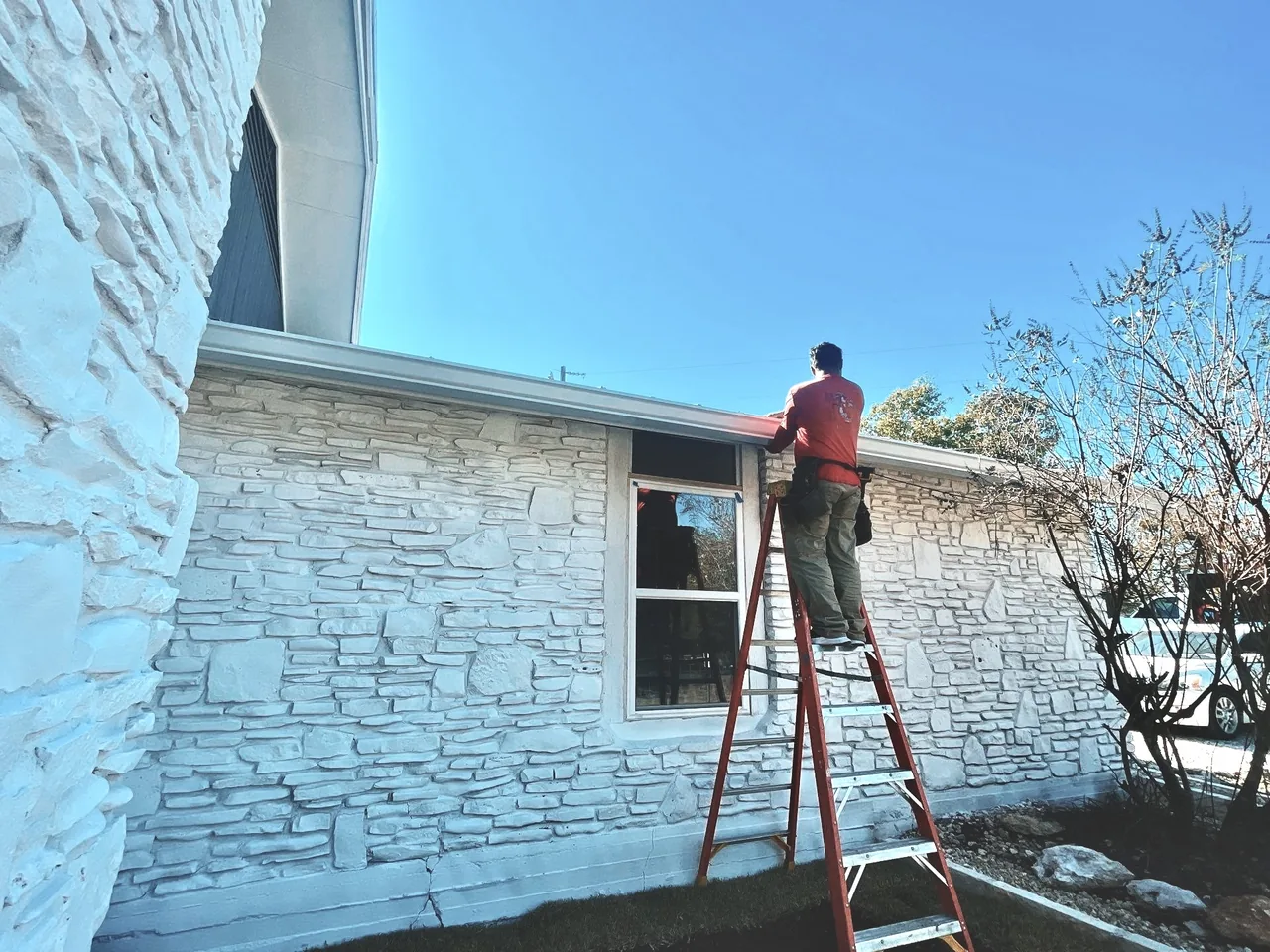 Urtiz crew member on ladder inspecting gutters and roofline on Texas stone home