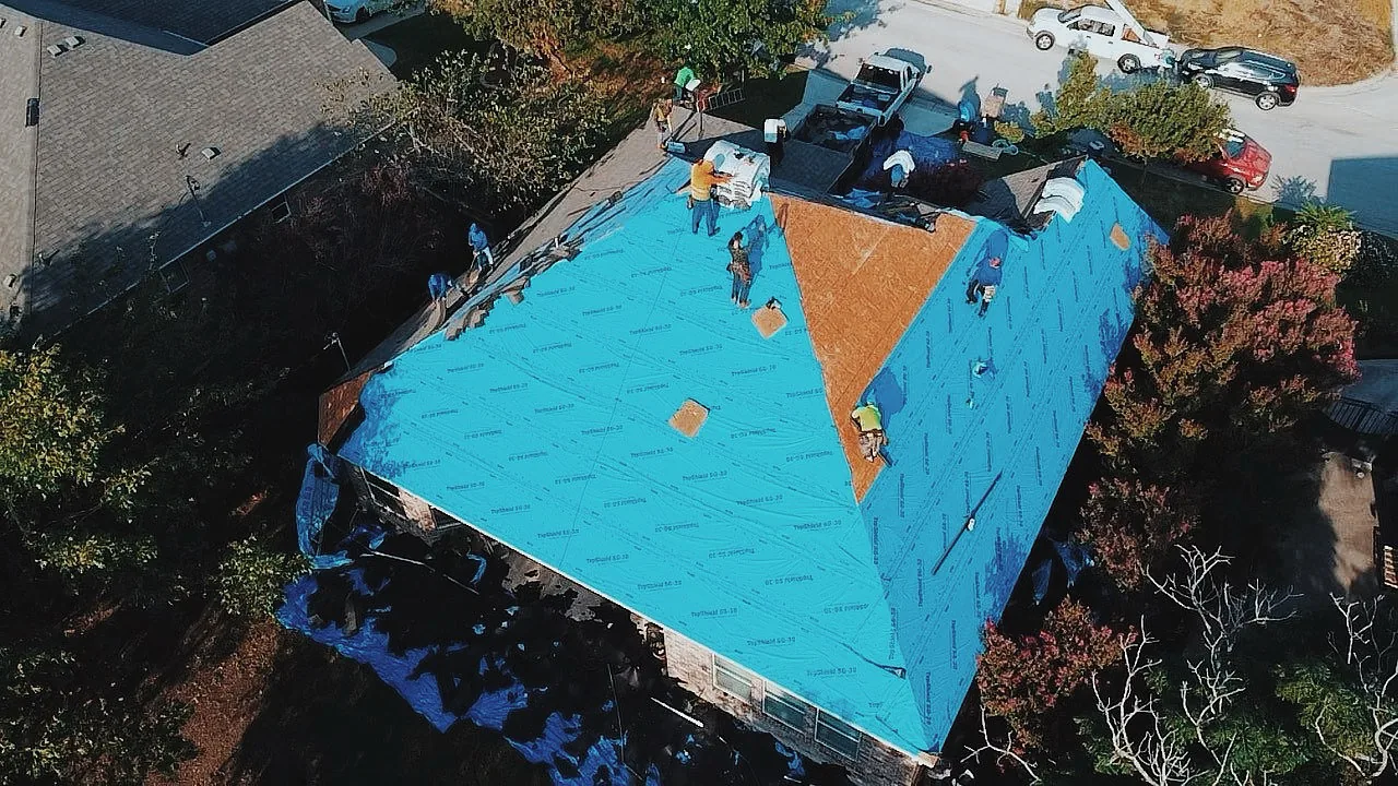 Crew installing blue synthetic underlayment on a roof during replacement